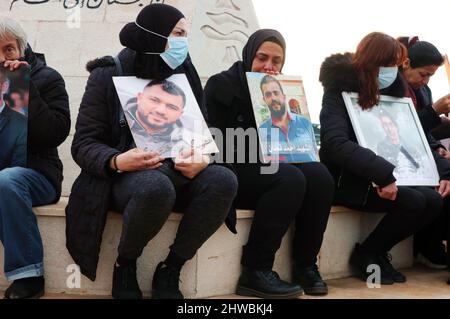 Beirut, Libanon. 04. März 2022. Familien von Opfern der Explosion versammeln sich vor der Auswandererstatue vor dem Hafen, um den 19.. Monat der Explosion zu markieren, Beirut, Libanon, März 4 2022. Die Familien protestieren gegen Beamte, die die Ermittlungen im Zusammenhang mit Hafensprengen behindern, die von Richter Tareq Bitar geleitet werden. Sie prangern auch den Willen der Regierung an, die verwüsteten Getreidesilos abzureißen, das heißt, mit ihren Worten, "die Erinnerung zu töten" an die Katastrophe. Die Demonstranten zeigen Portraits ihrer Lieben und halten ein Transparent mit der Aufforderung zur „Beseitigung von Hindernissen für die Ermittlungen und zur raschen Verhaftung von Kriminellen“. Stockfoto