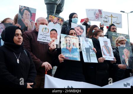 Beirut, Libanon. 04. März 2022. Familien von Opfern der Explosion versammeln sich vor der Auswandererstatue vor dem Hafen, um den 19.. Monat der Explosion zu markieren, Beirut, Libanon, März 4 2022. Die Familien protestieren gegen Beamte, die die Ermittlungen im Zusammenhang mit Hafensprengen behindern, die von Richter Tareq Bitar geleitet werden. Sie prangern auch den Willen der Regierung an, die verwüsteten Getreidesilos abzureißen, das heißt, mit ihren Worten, "die Erinnerung zu töten" an die Katastrophe. Die Demonstranten zeigen Portraits ihrer Lieben und halten ein Transparent mit der Aufforderung zur „Beseitigung von Hindernissen für die Ermittlungen und zur raschen Verhaftung von Kriminellen“. Stockfoto