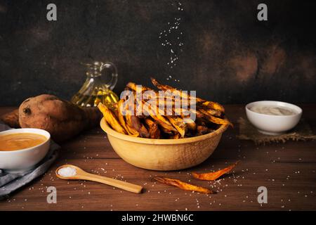 Köstliche und gesunde hausgemachte Süßkartoffelfrites, die in einer Luftfryer mit Saucen auf dunklem rustick-Hintergrund zubereitet werden Stockfoto