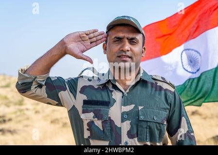 Armeeoffizier grüsst mit Blick auf die Kamera vor der winkenden indischen Flagge - ein Gespann von Patriotismus, Respekt und Stolz. Stockfoto