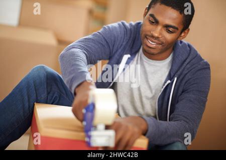 HES Umzug. Ein hübscher junger Mann, der Kisten verpackt. Stockfoto