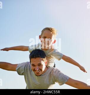 Lässt die Phantasie seiner Söhne aufsteigen. Aufnahme eines Vaters, der seinem Sohn an einem sonnigen Tag einen Huckepack gab. Stockfoto