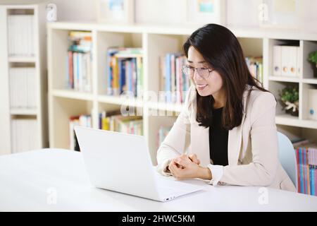 Moderne Büroangestellte Frau, die zu Hause oder im Büro freundlich lächelt und von zu Hause aus über das Internet online auf dem Laptop arbeitet Stockfoto