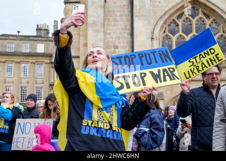 Bath, Großbritannien. 5.. März 2022. Eine Frau, die mit der ukrainischen Flagge drapiert ist, macht während einer Demonstration gegen die russische Invasion in der Ukraine ein Selfie vor der Abtei von Bath. Die Demonstration wurde organisiert, um den Menschen vor Ort zu ermöglichen, ihre Solidarität mit der Ukraine im Krieg zwischen Russland und der Ukraine zu zeigen und Putins Aktionen zu verurteilen. Quelle: Lynchpics/Alamy Live News Stockfoto