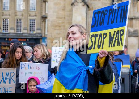 Bath, Großbritannien. 5.. März 2022. Eine Frau, die mit der ukrainischen Flagge gehisst ist, hält ein Anti-Putin-/Stopp-the-war-Plakat, während sie Reden vor der Abtei von Bath während einer Demonstration gegen die russische Invasion in der Ukraine hört. Die Demonstration wurde organisiert, um den Menschen vor Ort zu ermöglichen, ihre Solidarität mit der Ukraine im Krieg zwischen Russland und der Ukraine zu zeigen und Putins Aktionen zu verurteilen. Quelle: Lynchpics/Alamy Live News Stockfoto