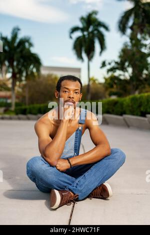 Er trägt Overalls und sitzt im Park Stockfoto