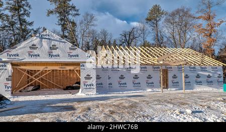 NISSWO, MN - 22 NOV 2021: Heimbaustelle im Winter, mit Tyvek Wrap, neuen Holzdachstühlen und Schnee auf dem Boden. Bäume säumen die BA Stockfoto