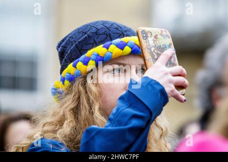 Bath, Großbritannien. 5.. März 2022. Eine Frau, die einen Hut in den Farben der ukrainischen Flagge trägt, wird abgebildet, während sie Reden vor der Abtei von Bath während einer Demonstration gegen die russische Invasion in der Ukraine hört. Die Demonstration wurde organisiert, um den Menschen vor Ort zu ermöglichen, ihre Solidarität mit der Ukraine im Krieg zwischen Russland und der Ukraine zu zeigen und Putins Aktionen zu verurteilen. Quelle: Lynchpics/Alamy Live News Stockfoto