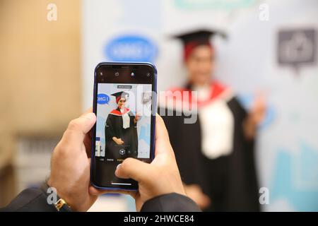 Eine hübsche asiatische weibliche Absolventin posiert für ein Familienfoto bei ihrer Abschlussfeier. Dieses formelle Ereignis, bei dem die Graduierung (vorher) in gr Stockfoto