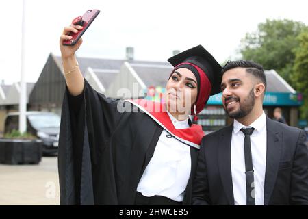 Eine asiatische Absolventin posiert mit ihrem Partner bei ihrer Abschlussfeier für Fotos. Dieses formelle Ereignis, bei dem sich die Graduierung (vor) ändert Stockfoto