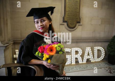 Eine hübsche asiatische Absolventin posiert mit einer Blumenbouque für Fotos bei ihrer Abschlussfeier. Dieses formelle Ereignis, bei dem die Graduierung (vor Stockfoto