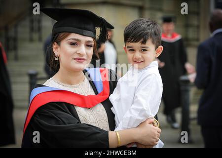 Eine hübsche asiatische Absolventin posiert für Fotos mit ihrem Sohn bei ihrer Abschlussfeier. Dieses formelle Ereignis, bei dem sich die Graduierung (vor) ändert Stockfoto