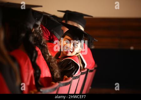 Eine hübsche asiatische weibliche Absolventin Posen wartet, um ihren Grad bei ihrer Abschlussfeier zu sammeln. Dieses formelle Ereignis, bei dem die Graduierung (vor) die Ganzzahl ändert Stockfoto