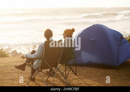 Die Aussicht von ihrem Campingplatz aus genießen. Eine kleine Aufnahme eines jungen Paares, das auf ihrem Campingplatz sitzt. Stockfoto