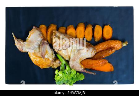 Blick von oben auf die gegrillten Wachteln teriyaki mit in Scheiben geschnittenen Karotten und Brokkoli auf Schwarz mit Board. Auf weissem Hintergrund Stockfoto