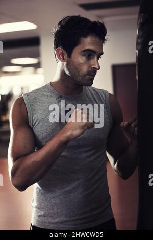 Es auf seinem Boxsack herausnehmen. Profil eines hübschen Mannes, der Sportkleidung trägt und bereit steht, im Fitnessstudio einen Boxsack zu schlagen. Stockfoto