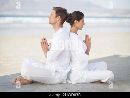 Yoga am Meer. Ein junges Paar, das am Strand Yoga praktiziert. Stockfoto