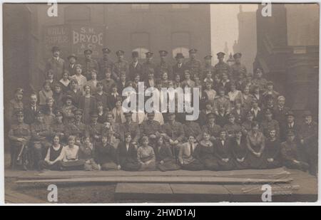 Futterkomitee, Priestley Hall, Leeds, Januar 1919. Gruppenfoto einer großen Anzahl von Männern und Frauen, die überwiegende Mehrheit der Männer sind in Armeeuniform. Auf dem Gebäude dahinter steht eine Werbetafel für S. M. Bryde & Co, Ltd., Tapetenhersteller. Das Frauenfrauenkorps unterstützte den Transport und die Versorgung von Pferden während des Ersten Weltkriegs Stockfoto