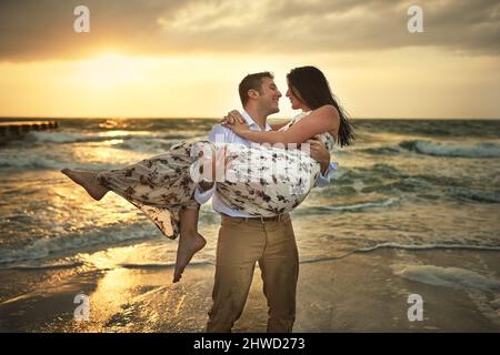 Ich lasse dich nie gehen. Kurzer Schuss eines hübschen jungen Mannes, der seine Freundin am Strand trägt. Stockfoto