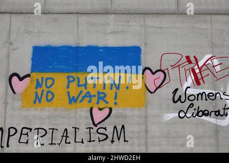 Graffiti der ukrainischen Flagge mit Antikriegsaufschriften auf einer grauen Betonwand in Prag. Stockfoto