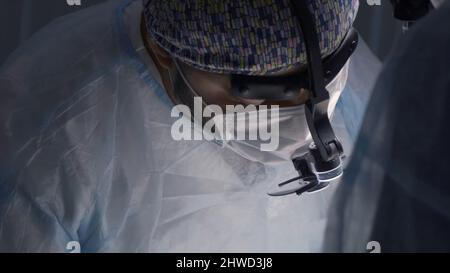 Ärzte in Masken und speziellen Brillen Durchführung der Operation. Aktion. Nahaufnahme von fokussierten Gesichtern von Chirurgen, die unter Anästhesie komplexe Operationen durchführen Stockfoto