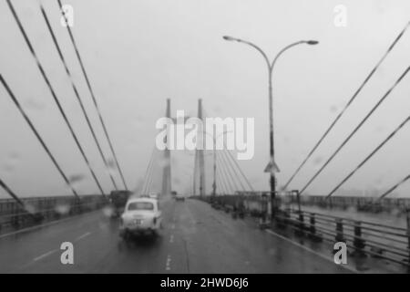 Verschwommenes Bild von Howrah, Westbengalen, Indien. Aufnahme durch Regentropfen, die auf die Windschutzscheibe des Autos fallen, nasses Glas, Verkehr an der Hoogly-Brücke 2.. Stockfoto