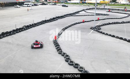 Kart-Rennfahrer in schützender roter Uniform und Helm bewegen sich auf der Strecke mit alten schwarzen Autoreifen. Kart-Fahrtraining. Stockfoto