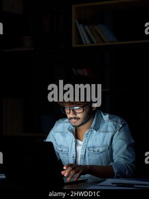 Junger indischer Geschäftsmann Student, der nachts mit einem Laptop online arbeitet. Stockfoto