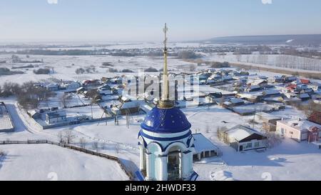 Nahaufnahme der blauen Kuppel und des goldenen Kreuzes der russisch-orthodoxen Kirche in der Nähe des kleinen Dorfes am klaren Wintertag. Religion und Glaube Stockfoto