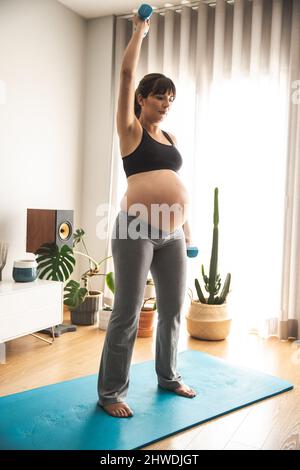 Schwangerin arbeitet zu Hause mit Hanteln. In guter Form bleiben, während Sie auf das Baby warten Stockfoto