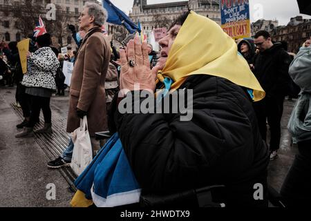 5.. März 2022, London, Großbritannien. Ukrainische Staatsbürger und pro-ukrainische Anhänger versammeln sich auf dem Trafalgar-Platz, um gegen die russische Invasion und den Krieg in der Ukraine zu protestieren. Ältere Frauen, die mit der ukrainischen Flagge drapiert sind, halten ihre Hände im Gebet zusammen. Stockfoto