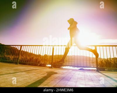 Sportler, der auf der Brücke läuft, Handlauf im Hintergrund. Abstraktes Licht, farbenfrohe Lichtreflexe. Stockfoto