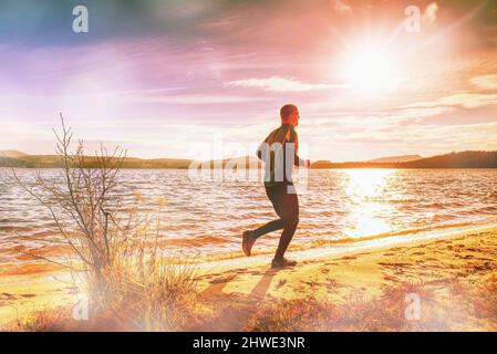 Großer Mann, der alleine den See runiining. Mann läuft am Strand. Abstraktes Licht, farbenfrohe Lichtreflexe. Stockfoto