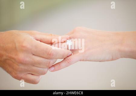 Die richtige finden - Ehe und Verlobung. Beschnittene Ansicht einer herrenhand, die einen Ehering auf einen Ring-Finger einer Frau schiebe. Stockfoto