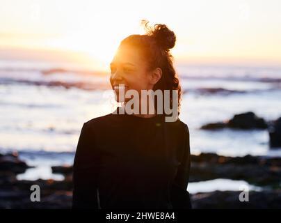 Ändere deine Gedanken und du veränderst dein Leben. Aufnahme einer attraktiven jungen Frau, die nach dem Yoga am Strand bei Sonnenuntergang alleine stand. Stockfoto