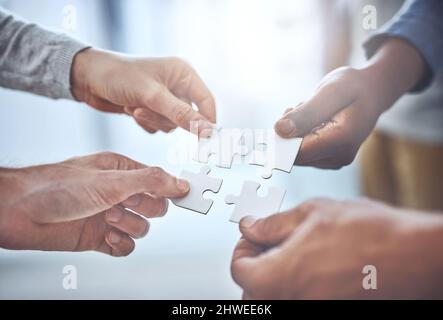 Wir können alles als Team lösen. Nahaufnahme einer Gruppe von nicht erkennbaren Geschäftsleuten, die Puzzleteile zusammenhalten. Stockfoto