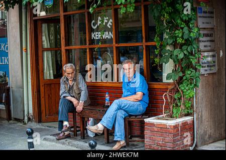 Zwei Männer mittleren Alters sitzen zusammen und unterhalten sich vor einem Café in Istanbul, Türkei. Stockfoto