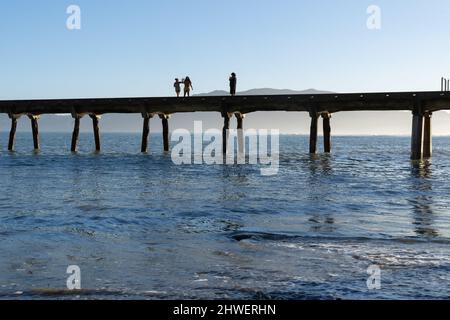 Tokomaru Bay New Zealand - Februar 4 2022; aus dem Meer Silhouetten von kleinen Figuren von drei Menschen halten Handys fotografieren Szene aus Stockfoto