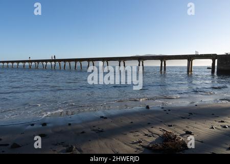 Tokomaru Bay New Zealand - Februar 4 2022; aus dem Meer Silhouetten von kleinen Figuren von drei Menschen, die entlang der langen historischen Wharf projiziert i Stockfoto