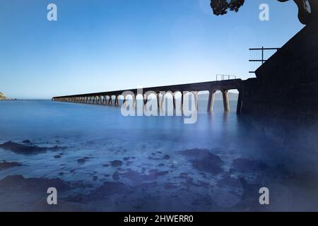 Die lange historische Tokomaru Bay Wharf ragt in die Bucht Stockfoto