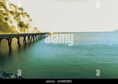 Sonnendurchflutete Klippen und historische Anlegestelle am Ende der Tokomaru Bay. Stockfoto