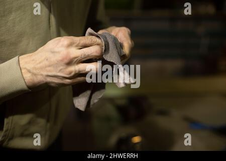 Wischen Sie das Teil mit einem Lappen ab. Lappen Sie sich in den Händen. Person reinigt den Mechanismus von Schmutz. Menschenhänden. Stockfoto