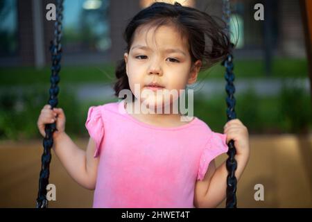 Mädchen auf Schaukel. Kind auf dem Spielplatz. Asiatische Vorschule Mädchen. Seilschaukel im Hof des Hauses. Mädchen in rosa Kleid ruht im Sommer. Stockfoto