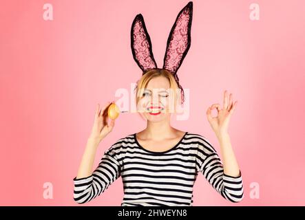 Ostertag. Bunny Mädchen mit gelbem Ei und Pinsel im Mund zeigt Schild ok. Eier dekorieren. Stockfoto