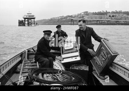 Drei einarmige Banditen, die für ein Wochenende in Clevedon, Somerset, gefestigt wurden, wurden mit dem Boot gerettet. Aber vier andere Spielautomaten mussten zurückgelassen werden, als abgehackte Meere den Betrieb zu gefährlich machten. Piermaster Bernard Faraway, 50 Jahre alt, leitete die Rettungsaktion. Der Pier-Kopf wurde vor einer Woche vom Festland abgeschnitten, als ein 200ft-Teilstück des Piers während der Sicherheitstests einstürzte. Eine vom Rat von Clevedon angeordnete Umfrage wird durchgeführt, um zu entscheiden, ob der 1000ft lange Pier repariert oder abgerissen werden soll. Bernard ist mit Roy Lovelock und Bill Cooke abgebildet. 23.. Oktober 1970. Stockfoto