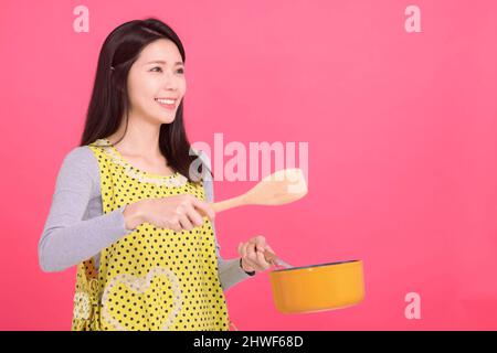 Glückliche junge Frau Hausfrau trägt Küchenschürze beim Kochen Stockfoto