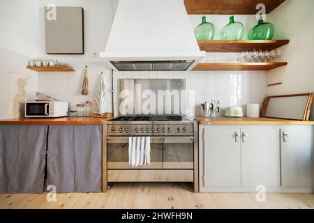 Schöne Einbauküche mit Holzarbeitsplatte, Gasherd mit Öfen und großer Dunstabzugshaube mit weichen Holzplatten und Geschirr darauf Stockfoto