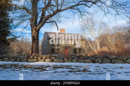 Das Jacob Whittemore House im Winter, hinter einer Steinmauer, umgeben von blattlosen Bäumen. Minute man National Historical Park, Lexington, MA. Stockfoto