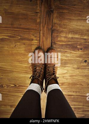 Rustikaler Stil. POV-Aufnahme einer Person, die Stiefel trägt und auf einem Holzboden steht. Stockfoto