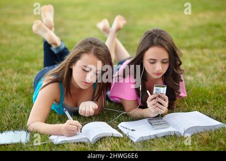 Beste Knospen, in der Schule und draußen. Teenager-Mädchen liegen zusammen auf einem Rasen und machen ihre Hausaufgaben. Stockfoto